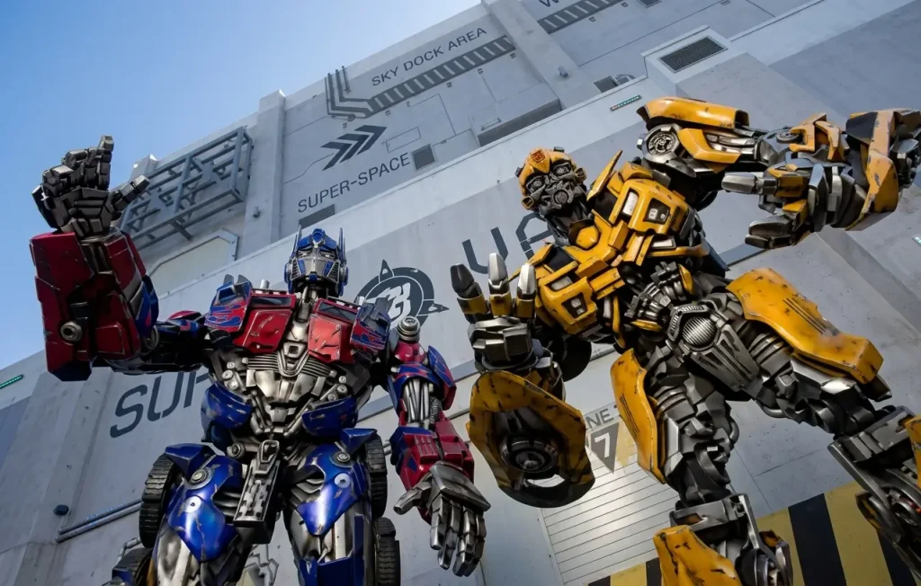 Transformers robot characters in red, blue and yellow posed outside a white ride building