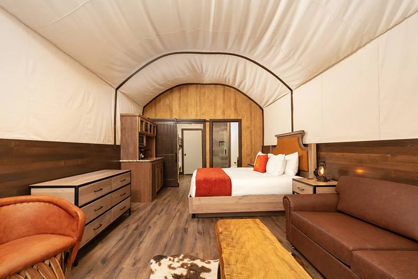 Interior of a Westgate River Ranch Resort luxe Conestoga wagon with a canvas ceiling, bed, sofa and cowhide rug