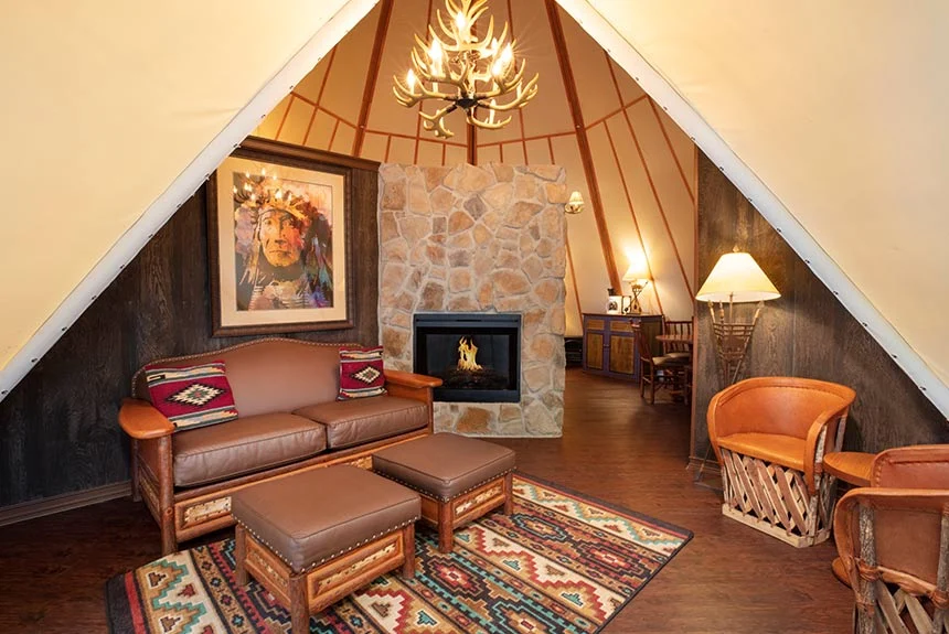 Living area in a Westgate River Ranch Resort luxe teepee with a leather sofa, stone fireplace and southwestern rug