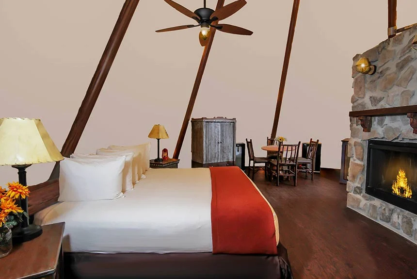 Bed with white and red bedding next to a stone fireplace and ceiling fan in a Westgate River Ranch Resort luxe teepee