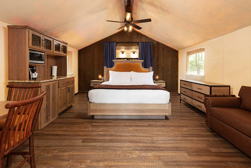 Interior of a Westgate River Ranch Resort luxury glamping tent with a bed, ceiling fan, wood cabinetry and a sofa