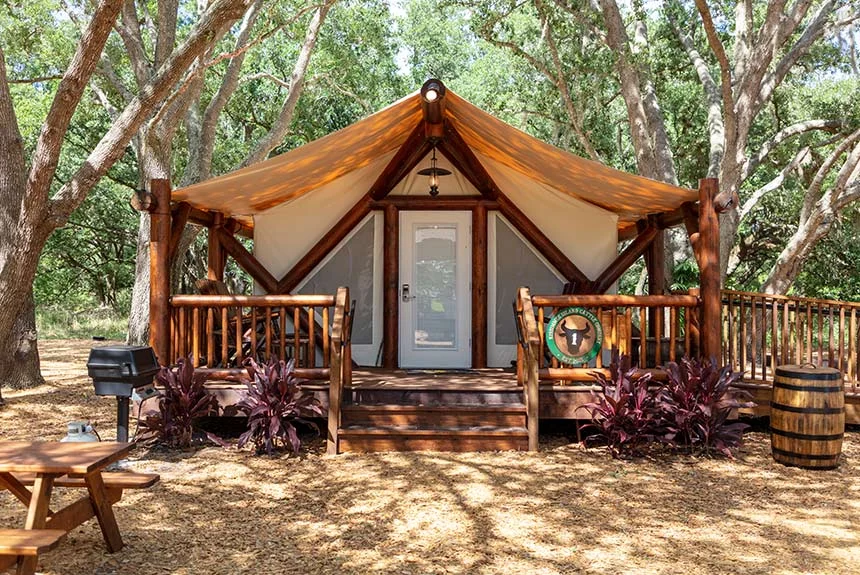 Luxury glamping tent at Westgate River Ranch Resort with a wooden porch, grill and picnic table under shade trees
