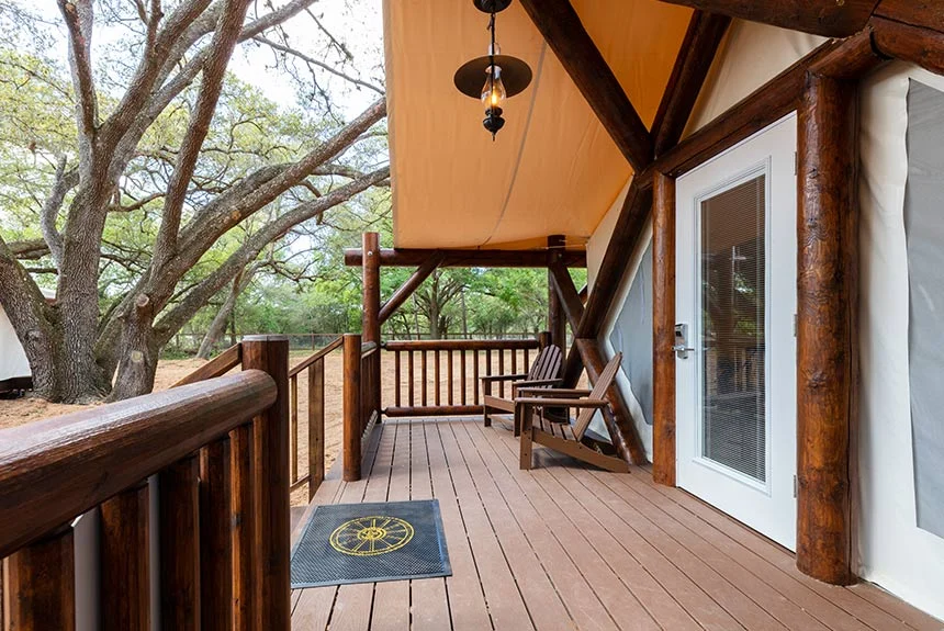 Covered wooden porch of a Westgate River Ranch Resort luxury glamping tent with a chair and a view of oak trees