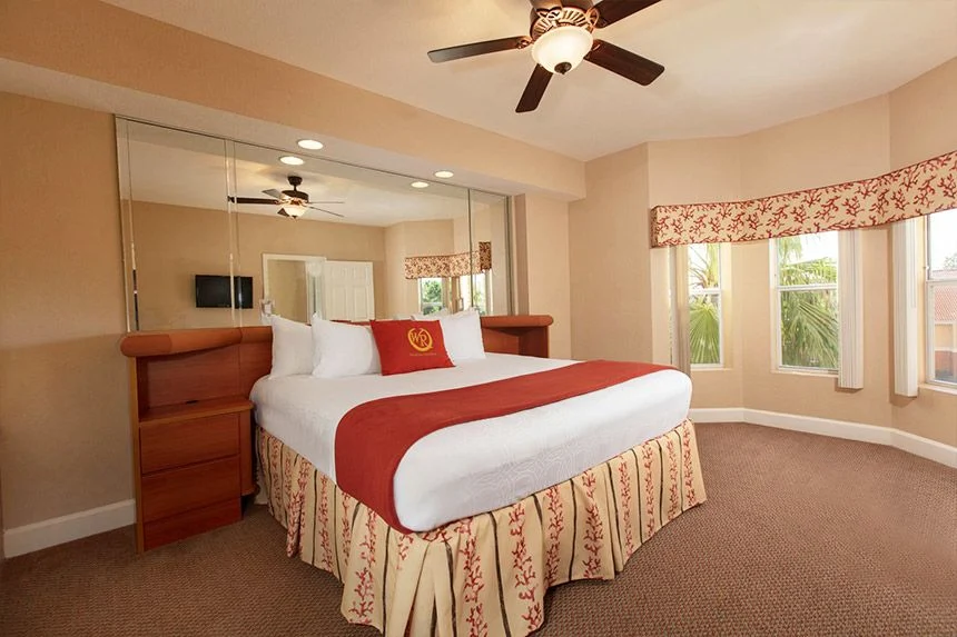 Westgate Town Center Resort one-bedroom deluxe villa bedroom with a bed, mirrored closet doors and valanced windows