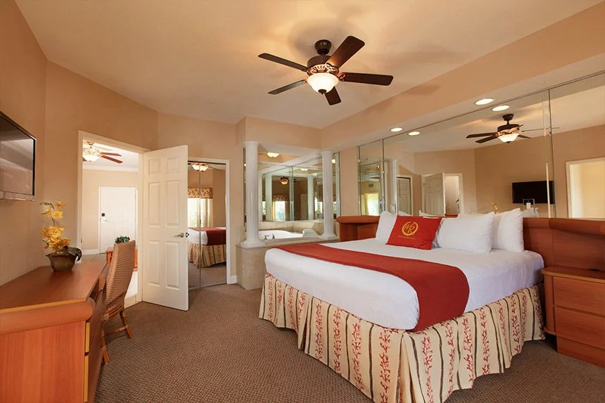 Bedroom of a Westgate Town Center Resort one-bedroom deluxe villa with a red throw, desk and mirrored closet doors