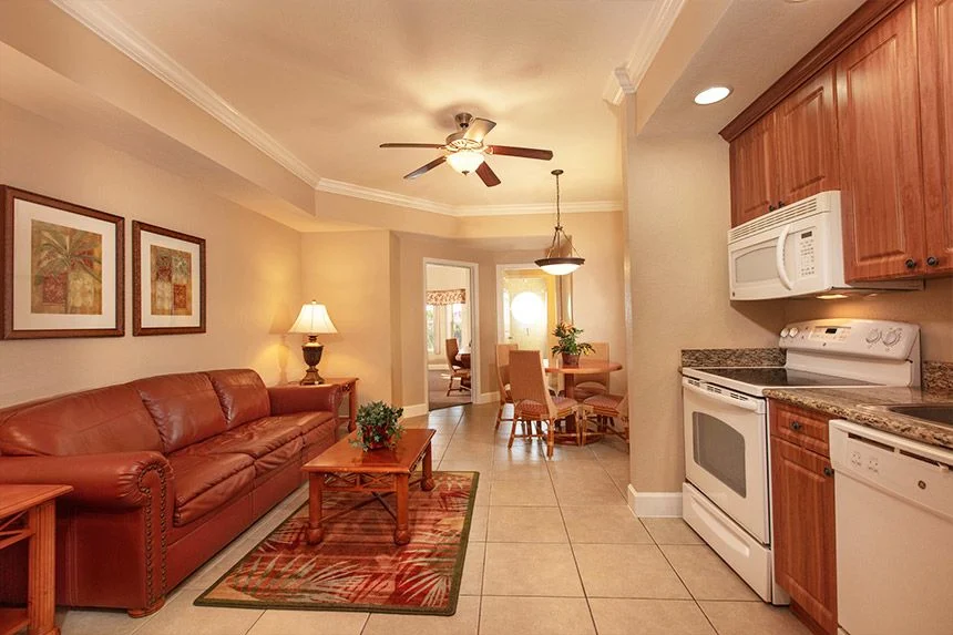 Living room and kitchen of a Westgate Town Center Resort one-bedroom deluxe villa with a leather sofa and white appliances