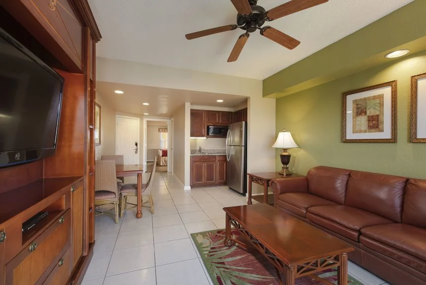 Living area of a Westgate Town Center Resort studio deluxe with a leather sofa, entertainment center and kitchenette beyond