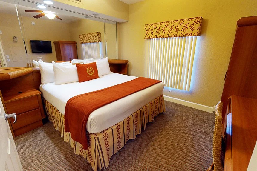 Bedroom of a Westgate Town Center Resort one-bedroom villa with a red throw, mirrored closet doors and a TV