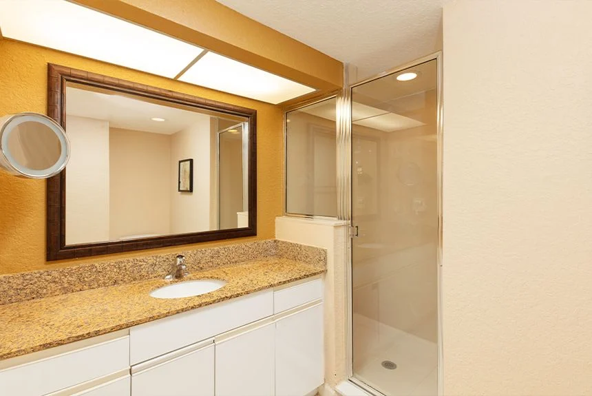 Bathroom of a Westgate Vacation Villas Resort studio with a granite vanity, framed mirror and glass shower