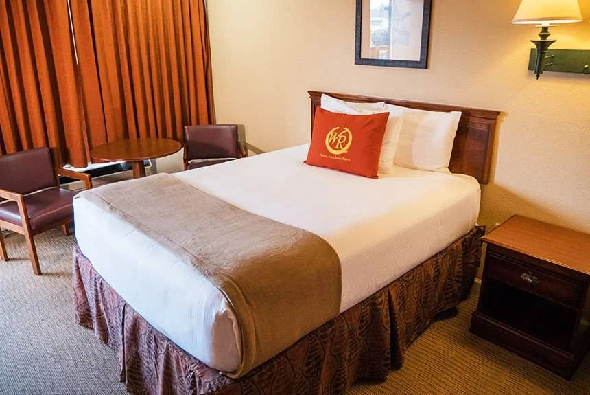 Queen bed, nightstand and chairs by a curtained window in a Wild Bear Inn double queen poolside guest room