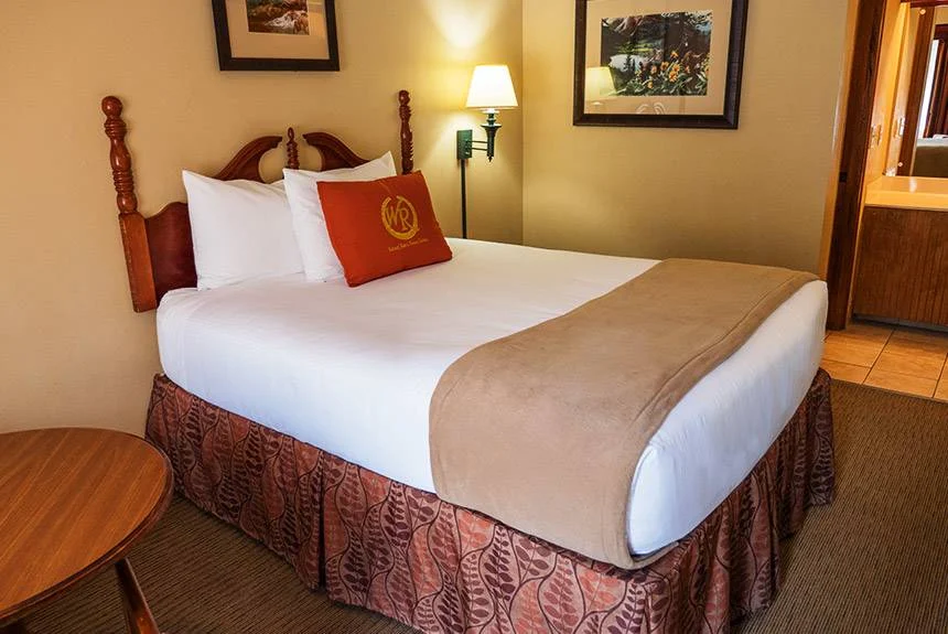 Wild Bear Inn queen guestroom with a wooden bed, red accent pillow, framed art and a wall lamp