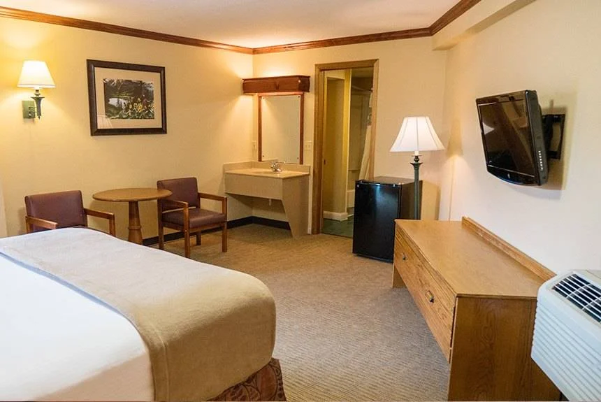 Wild Bear Inn queen poolside guest room with a wall-mounted TV, dresser, small table with chairs and vanity area