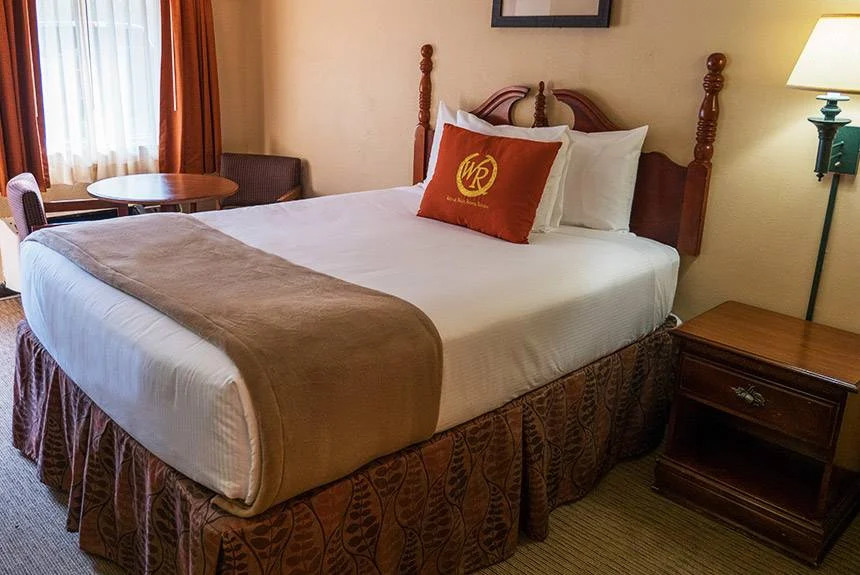 Wild Bear Inn queen guestroom with a wooden four-poster bed, red accent pillow and a small table by the window