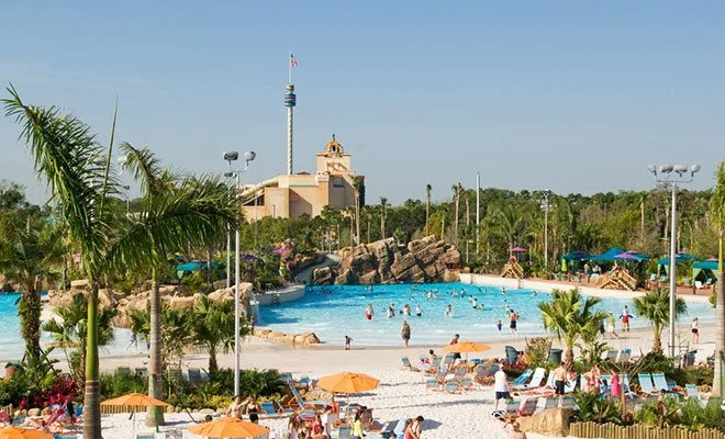 Sandy wave pool beach with swimmers, palm trees and umbrellas at Aquatica water park in Orlando