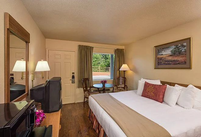 King bed, round table by the window and a dresser with TV in a Westgate Branson Woods Hotel king room