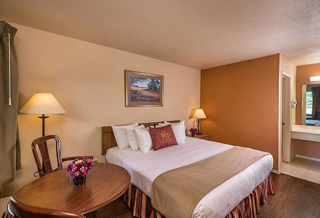 King bed, orange accent wall and a round table with flowers in a Westgate Branson Woods Hotel king room