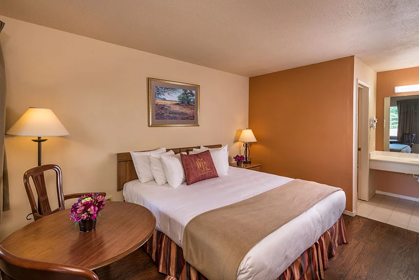Hotel room at Westgate Branson Woods Hotel with a bed, orange accent wall and a round table with flowers
