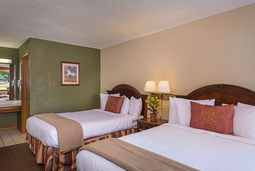 Two beds with red pillows, a green accent wall and an open vanity area in a Westgate Branson Woods Hotel room