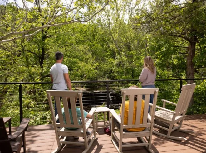 Couple standing at the railing of a wooden deck with rocking chairs overlooking a forest in Branson