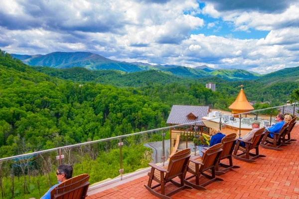Visitors in wooden rocking chairs on a hilltop deck overlooking forested Smoky Mountain ridges