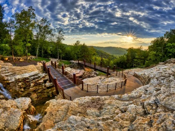 Wooden walkway winding through rocky limestone terrain toward wooded hills at sunset in Branson