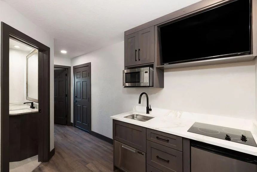 Kitchenette with dark cabinets, microwave, sink and cooktop below a wall TV in a Westgate Park City Resort & Spa studio