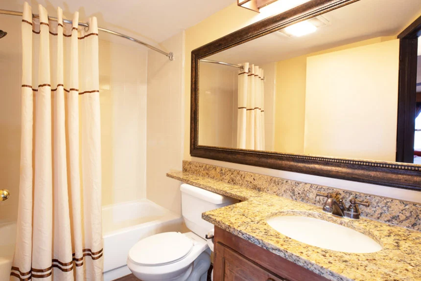 Bathroom of a Westgate River Ranch Resort deluxe lodge suite with a granite vanity, large mirror and curtained tub