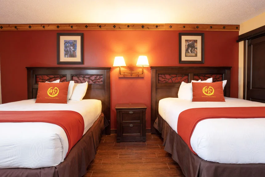 Two beds with red and white bedding separated by a nightstand in a Westgate River Ranch Resort deluxe lodge suite