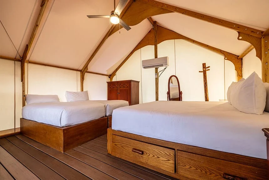 Inside a Westgate River Ranch Resort glamping tent with two beds, a ceiling fan and a wall-mounted air conditioner
