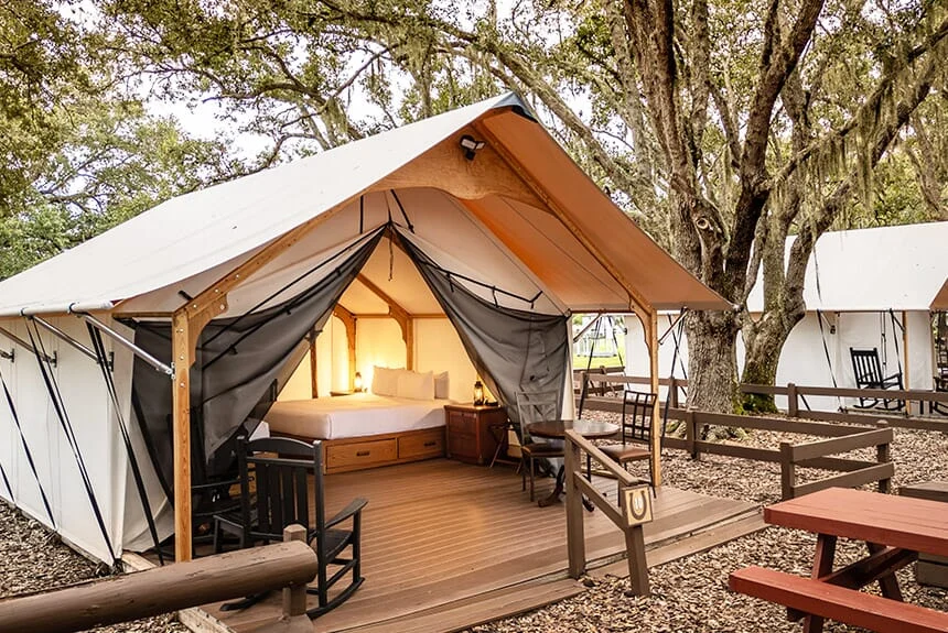 Westgate River Ranch Resort glamping tent with open canvas flaps, a wooden deck with rocking chairs and a picnic table