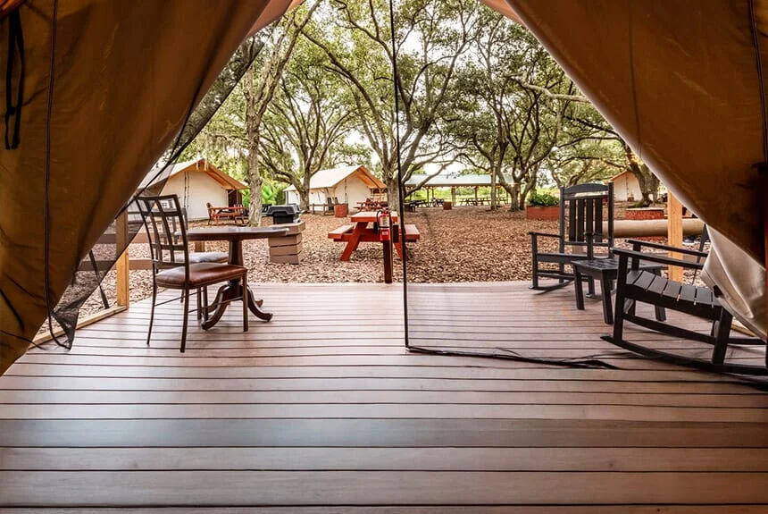 View from inside a Westgate River Ranch Resort glamping tent onto a wooden deck with a table, chairs and tents beyond