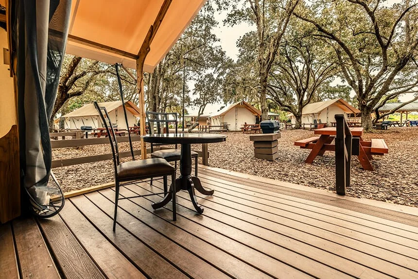 Wooden deck of a Westgate River Ranch Resort glamping tent with a bistro table and chairs overlooking tents under oak trees