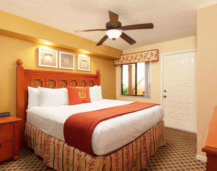 Bedroom of a Westgate Town Center Resort two-bedroom villa with a carved headboard, red accent pillow and ceiling fan