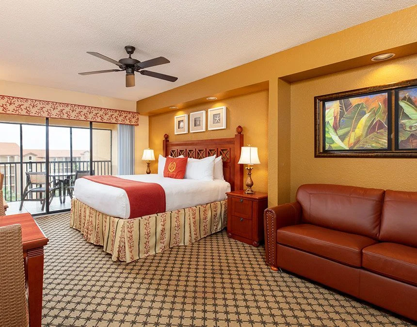 Westgate Town Center Resort studio with a bed, leather sofa, tropical painting and a door to the balcony