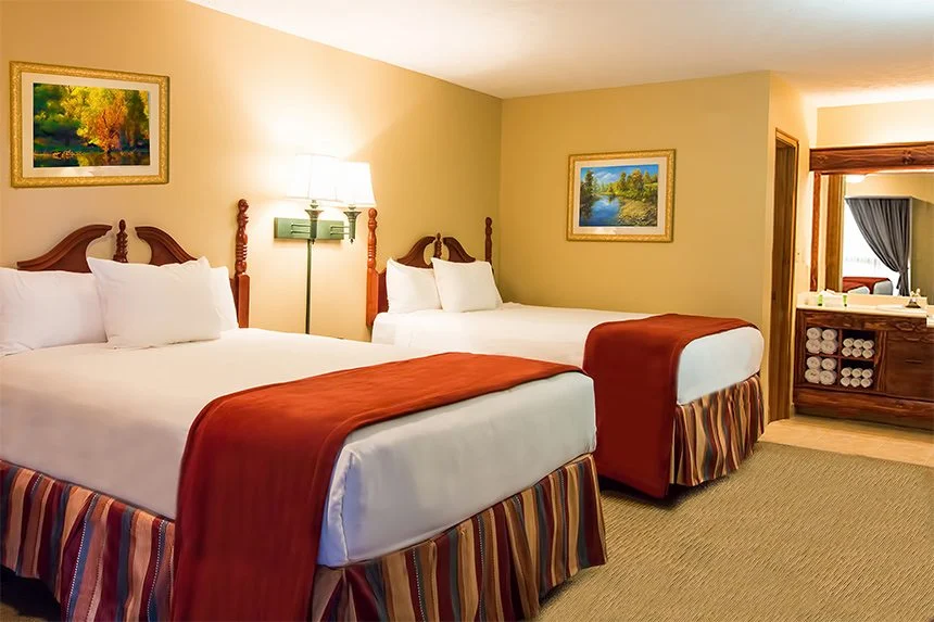 Wild Bear Inn hotel room with two beds in red and white bedding, landscape paintings and a vanity area
