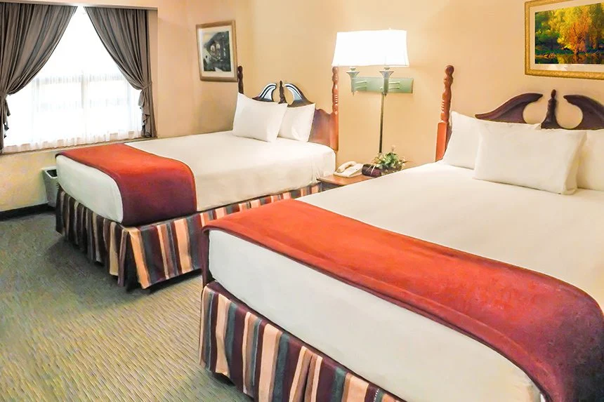 Two beds with red throws beside a curtained window and floor lamp in a Wild Bear Inn hotel room