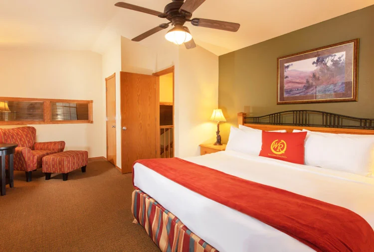 Bedroom of a Westgate Branson Woods two-bedroom villa with a bed, red throw and an armchair with ottoman