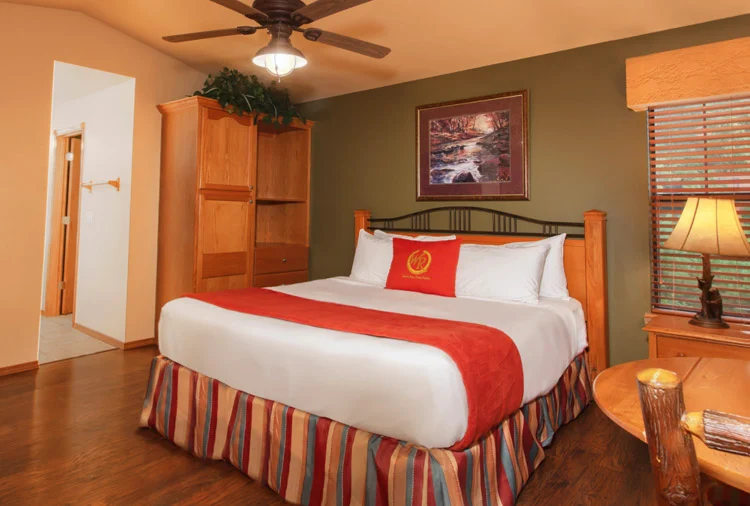 Bedroom in a Westgate Branson Woods two-bedroom villa with a bed, striped bed skirt, wood armoire and wood floors