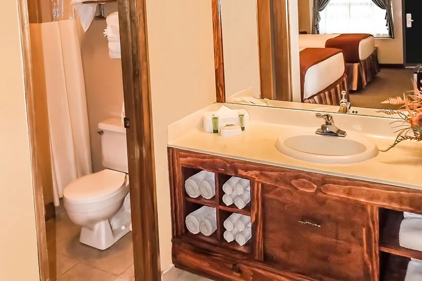 Wild Bear Inn hotel room vanity with rolled towels, a mirror reflecting the bed and a toilet beyond