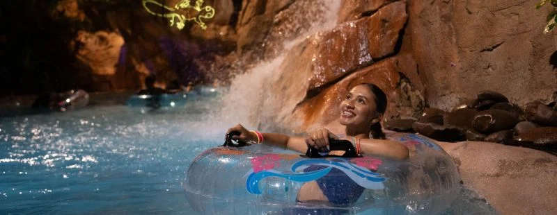 Woman floating on a tube past a lit waterfall on Aquatica Orlando's lazy river at night