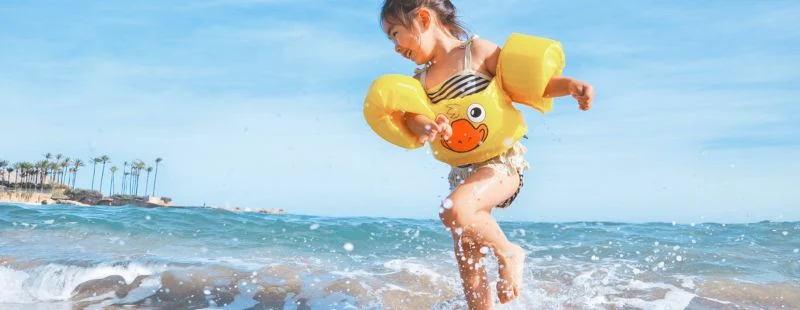 Child in duck-print arm floaties jumping through the surf at the beach