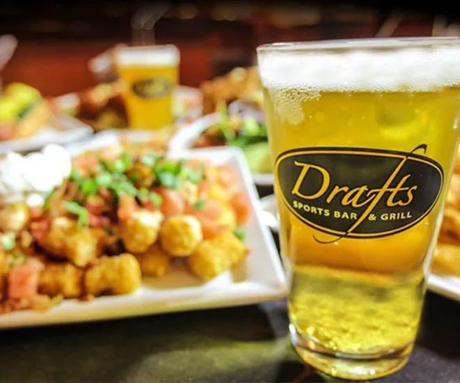 Glass of beer with the Drafts Sports Bar & Grill logo beside a plate of loaded tater tots
