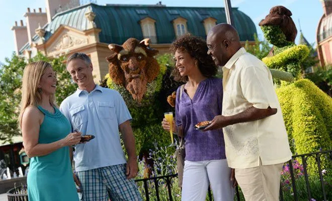 Two couples chatting over drinks and snacks beside a Beast topiary at EPCOT