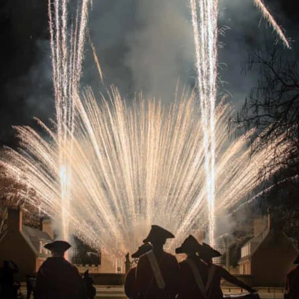 Fireworks bursting behind silhouettes of people in tricorn hats at night