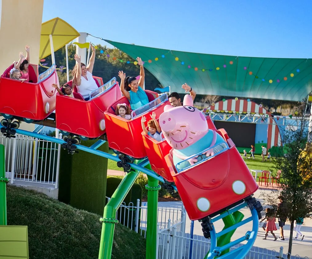 Riders raising their arms on a red coaster car at Peppa Pig Theme Park Florida