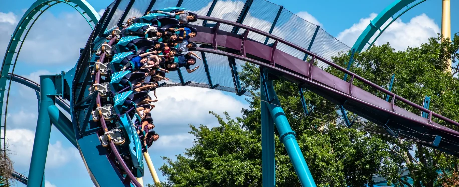 Riders on a teal roller coaster rounding a curve among trees