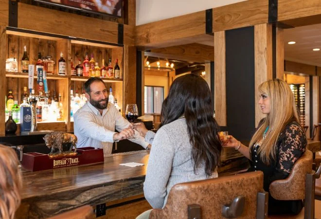 Bartender handing a glass of red wine across the wooden bar to guests at River Ranch Cattle Company