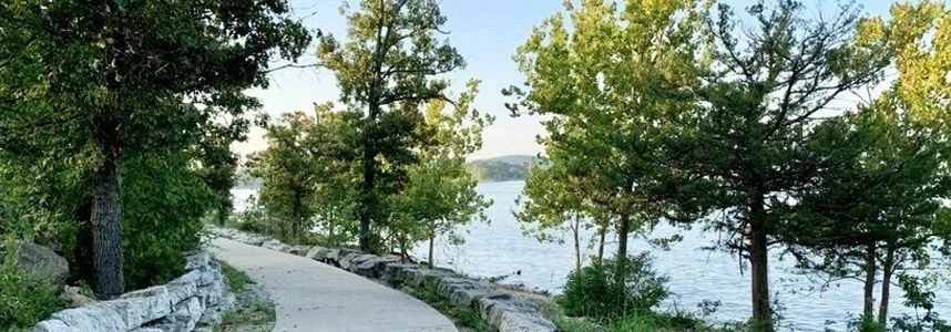 Paved trail winding along a lakeshore beneath leafy trees in Branson