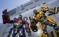 Transformers robot characters in red, blue and yellow posed outside a white ride building