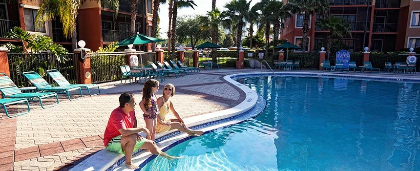 Couple sitting at the edge of the pool with lounge chairs and palms at Westgate Lakes Resort & Spa